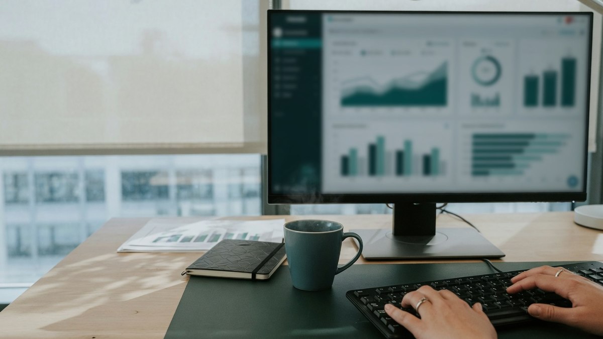 Bureau professionnel avec écran d'ordinateur affichant un tableau de bord de statistiques web, mains sur un clavier hors champ, sans visage identifiable