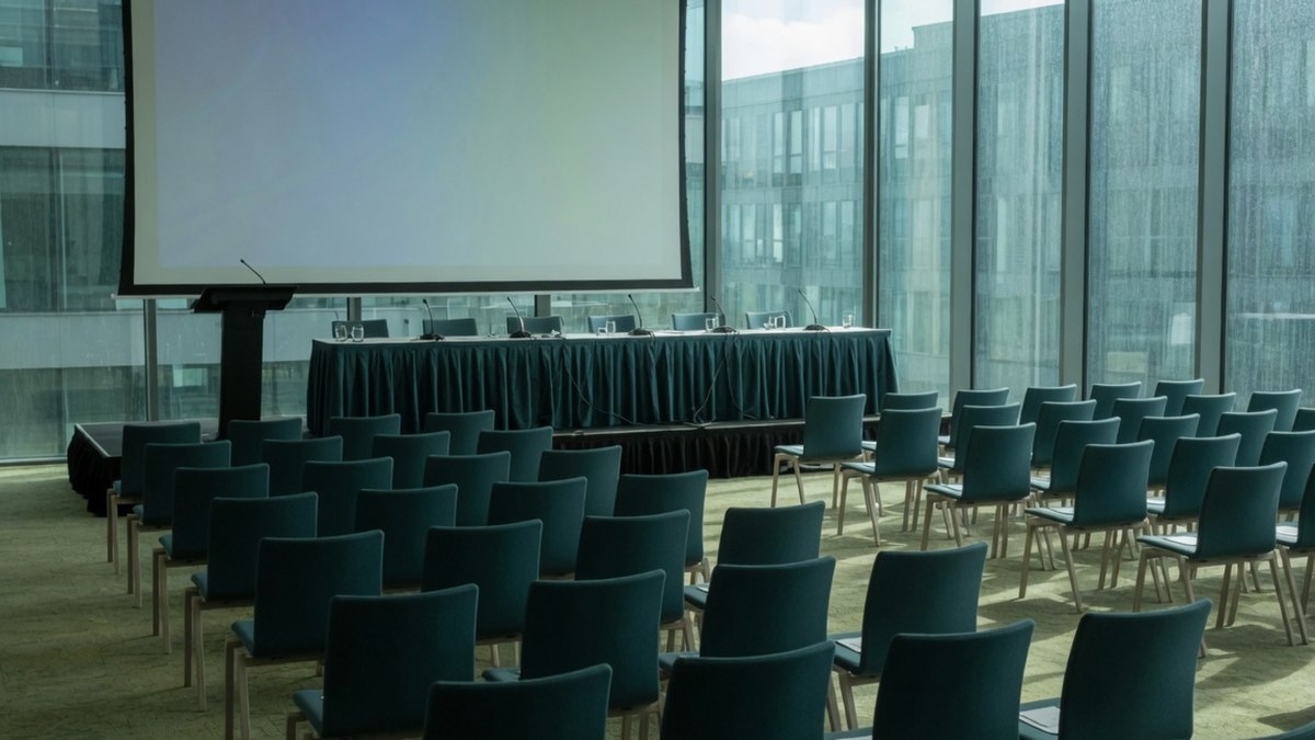 Rangées de chaises vides face à un écran de projection dans une salle de conférence avant un événement professionnel